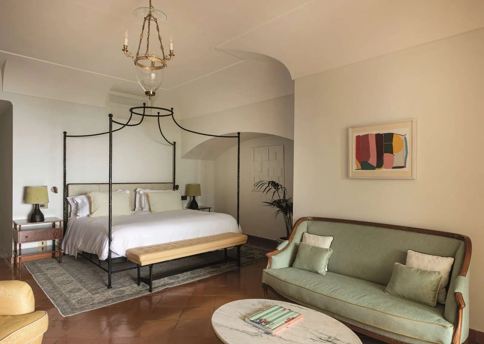 Sea View Suite with Garden at Caruso, A Belmond Hotel: an iron four poster bed, a green sofa and a marble coffee table on a terracotta floor