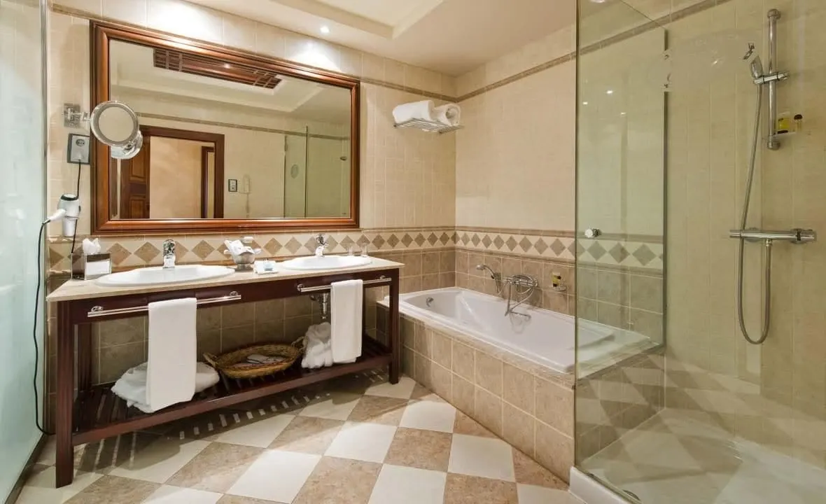 Deluxe double room with view of golf course at Elba Palace Golf Boutique Hotel: a bathroom with twin basins, a bath and a separate glass shower