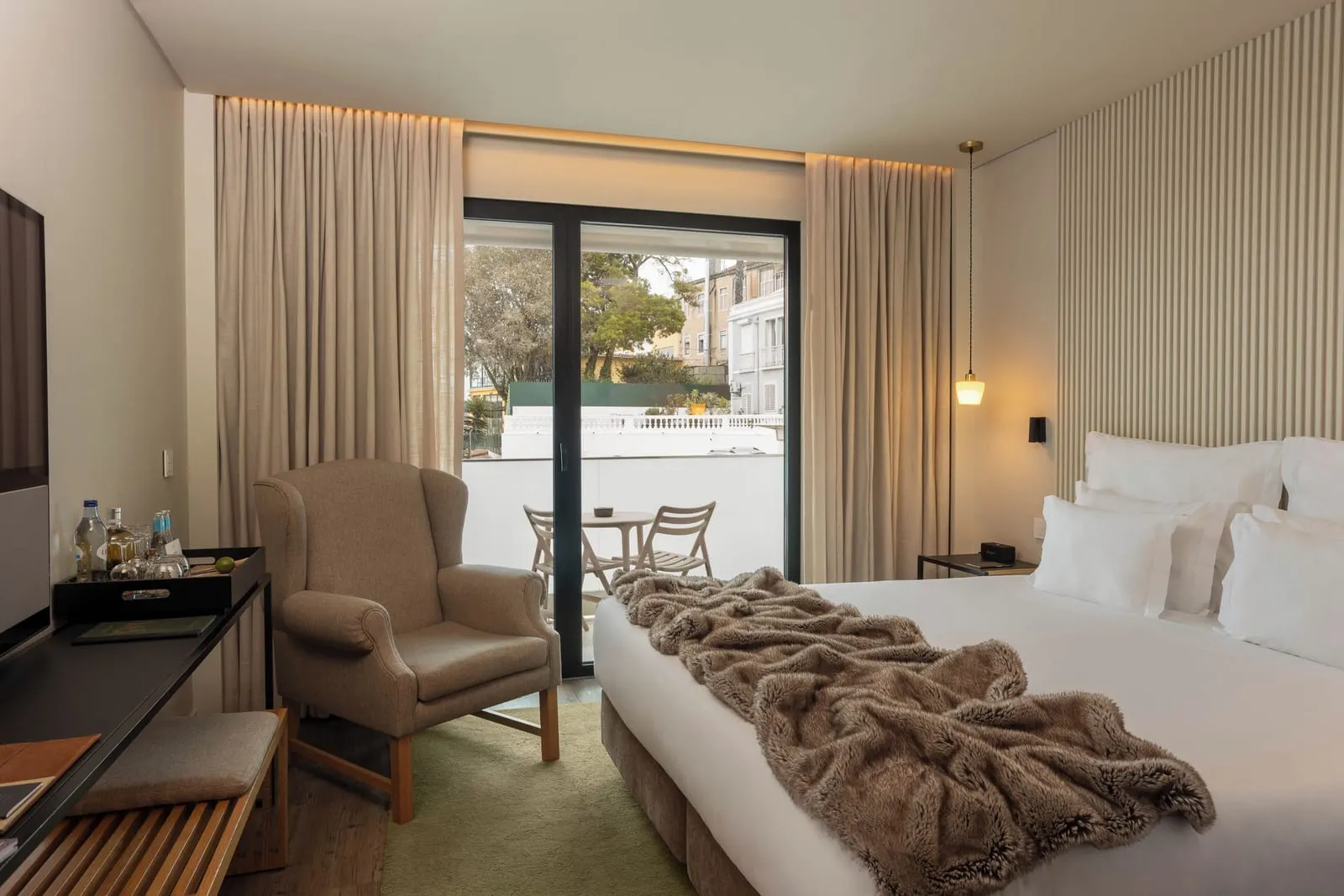 Superior Room at Memmo Príncipe Real: the bed, an armchair and glass doors to an outdoor table and chairs