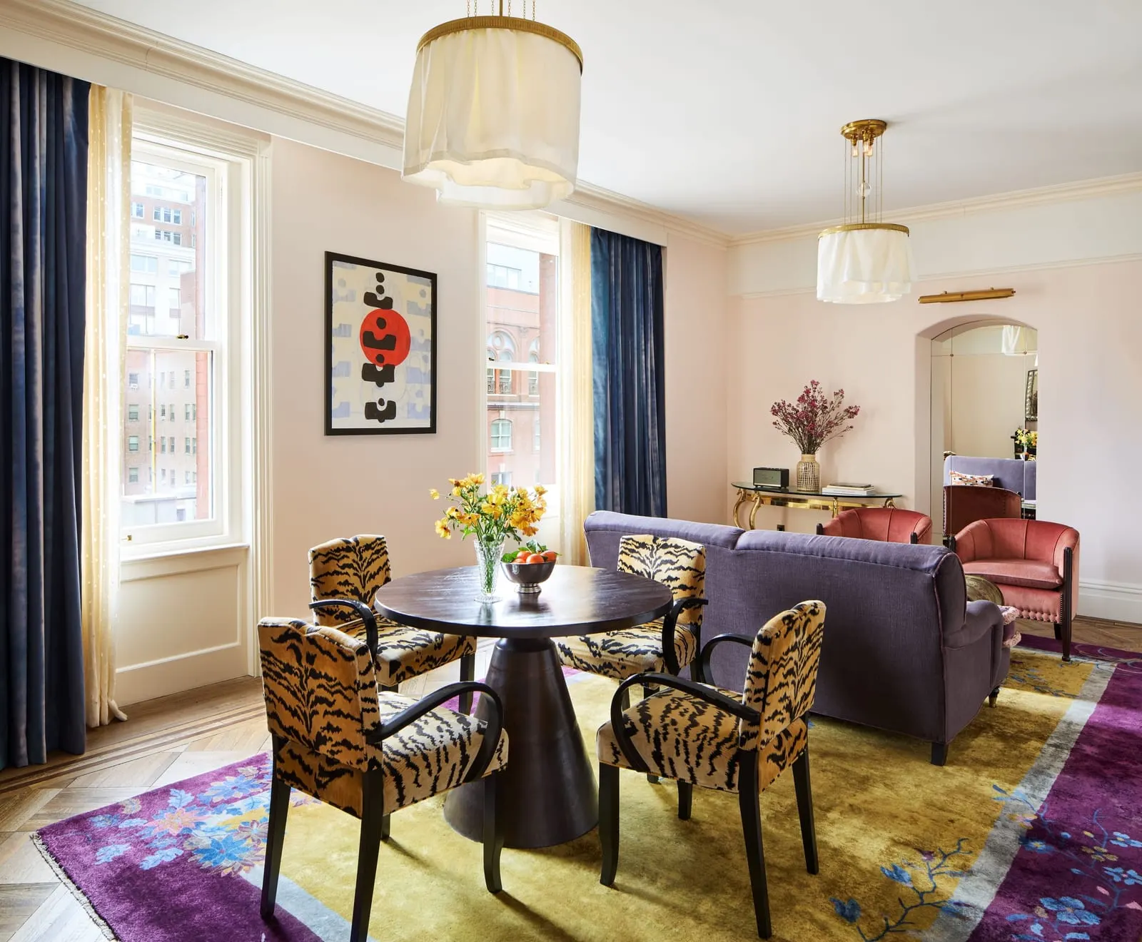 Chelsea Grand Suite at Hotel Chelsea: a round dining table with four tiger-print chairs beside two tall windows, with a purple sofa and pink armchairs in the living area beyond