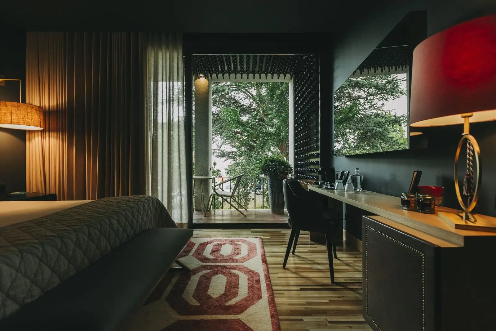 Executive Superior Room at Torel Avantgarde: the bed, a desk with a red lamp and glass doors to a balcony among trees