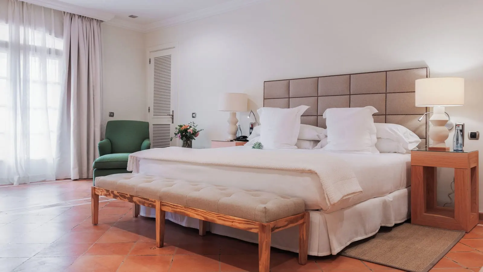 Junior Suite at Bahía del Duque: a king bed with a padded headboard, a bench at its foot and a green armchair