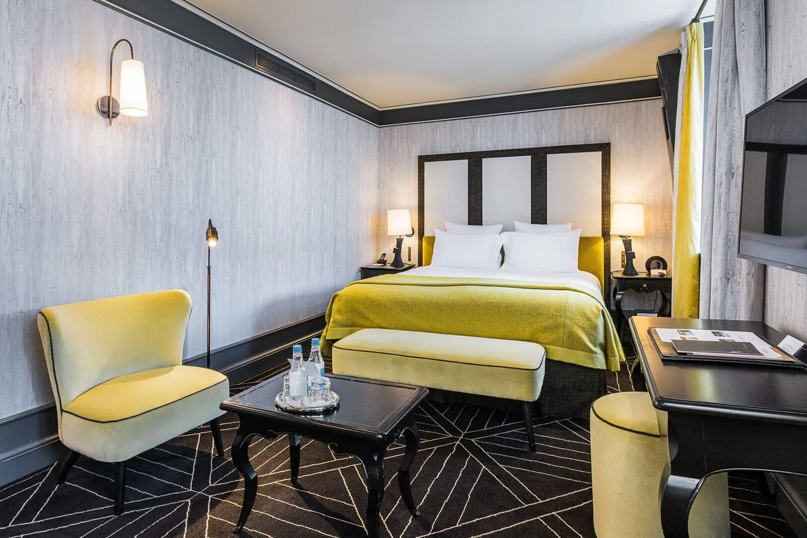 Deluxe Room at Le Pavillon de la Reine: a double bed with a yellow throw and a matching bench, a velvet armchair, a coffee table and a writing desk