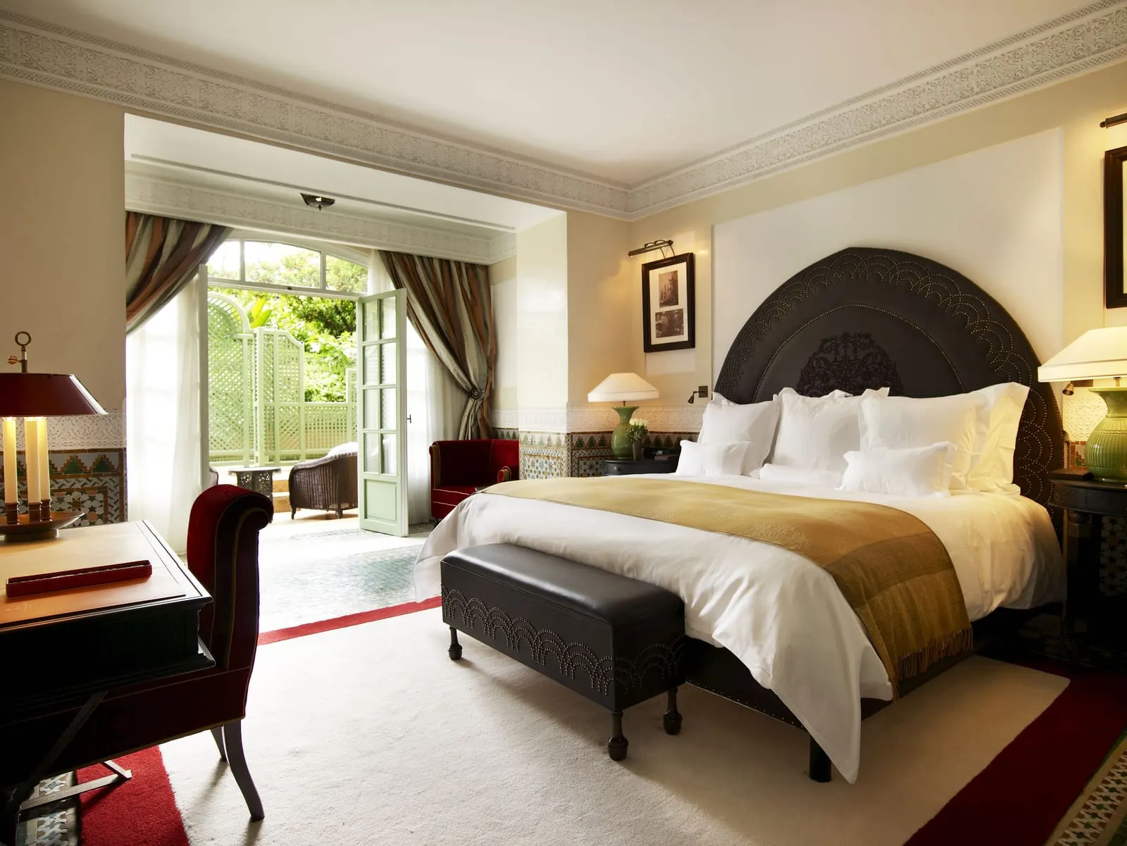 Duplex Suite at La Mamounia: a king bed under a dark carved headboard, with doors open to a private terrace