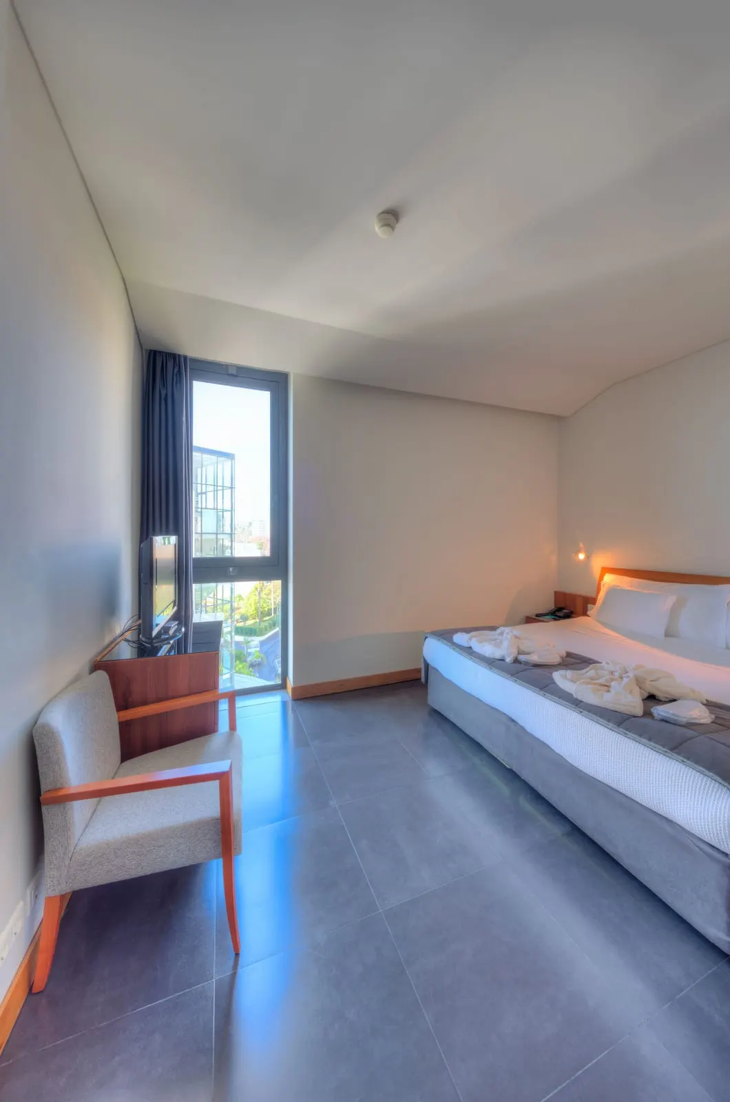 VidaMar Resort Hotel Madeira Premium Sea View Suite：キングサイズのベッド、アームチェア、背の高い横の窓がある寝室