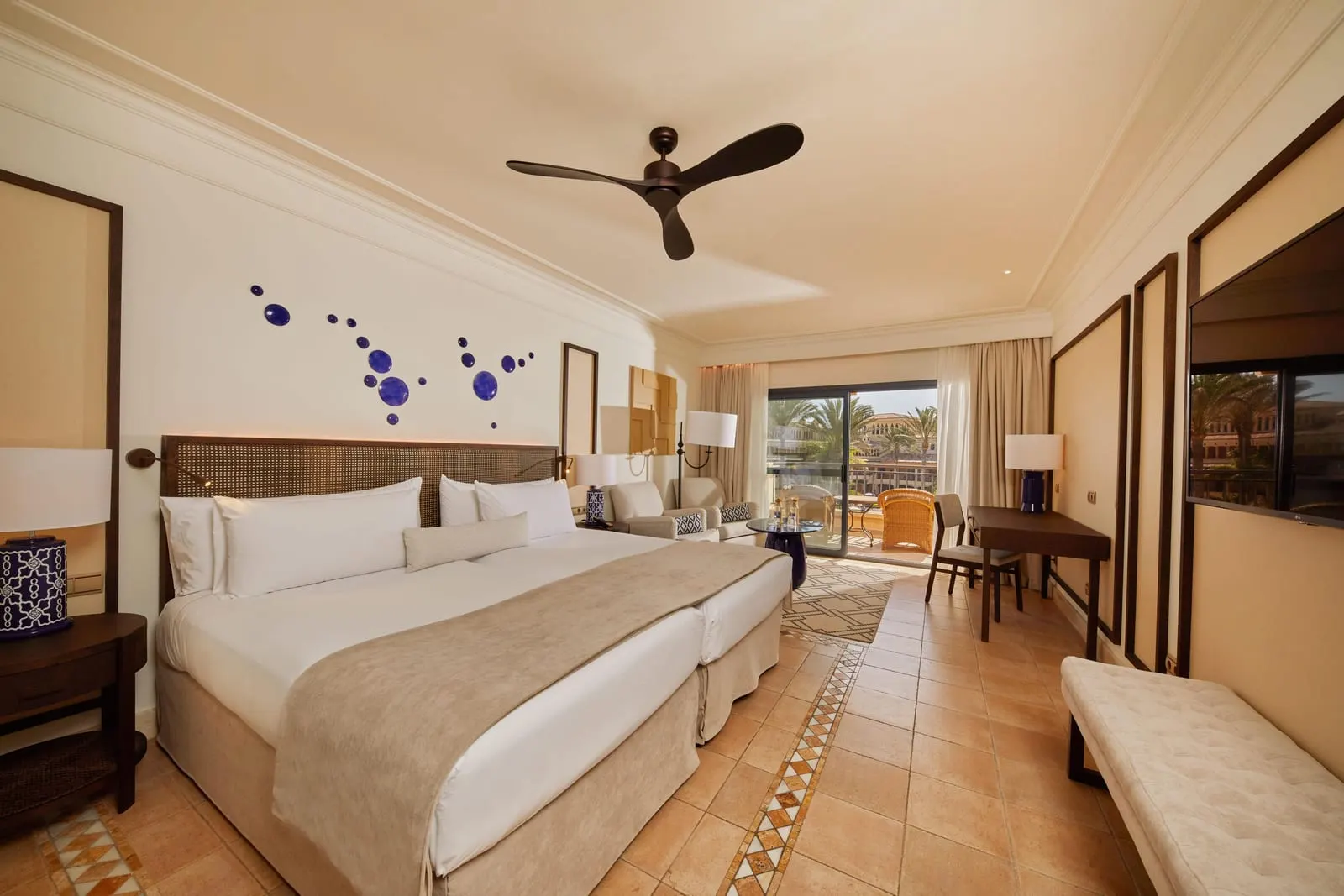 Junior Suite Pool View at Secrets Bahía Real Resort & Spa: two single beds made up side by side under a ceiling fan, with a desk, a sitting area and a sliding door to the balcony
