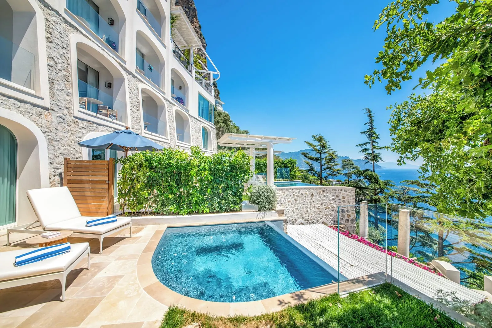 Deluxe Suite Sea View & Pool at Borgo Santandrea: a private pool on a terrace with loungers, a lawn and a glass balustrade beside the building.