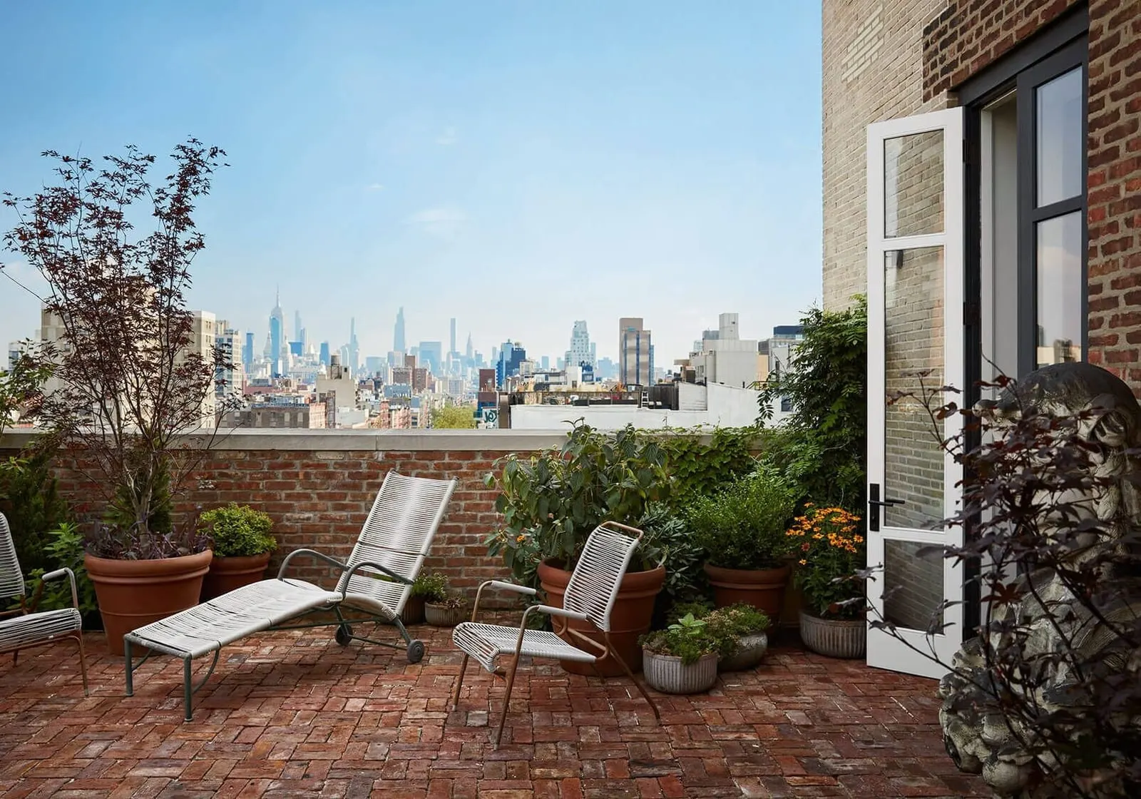 Terrace Suite at Nine Orchard: a brick-paved terrace with two metal loungers and potted plants, with the city skyline in the distance