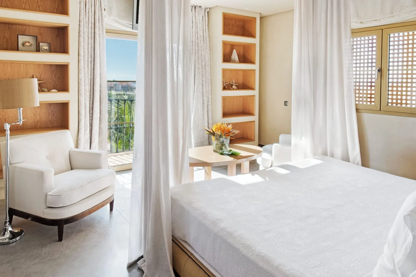 Villa Las Retamas at Bahía del Duque: the bed with white curtains, an armchair, shelving and a door to the balcony