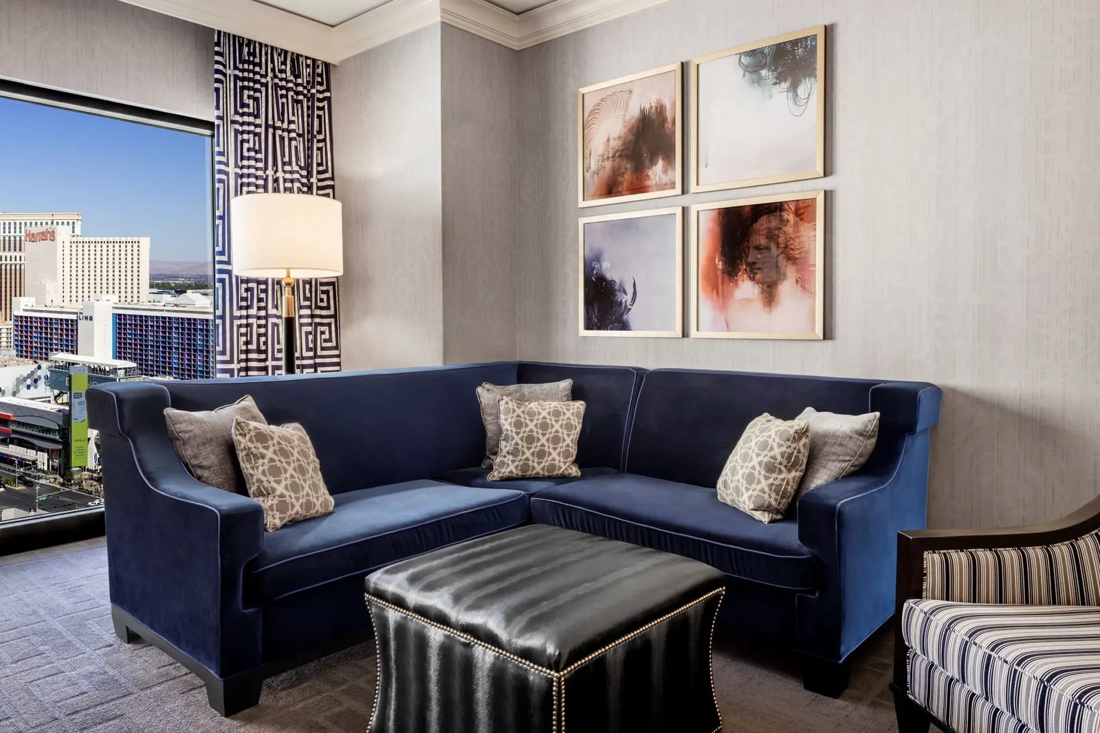 Augustus Premium Room im Caesars Palace, wie das Zimmer vor dem Umbau 2026 aussah: ein blaues Ecksofa, ein Lederhocker, ein gestreifter Sessel und gerahmte Drucke an einem Fenster