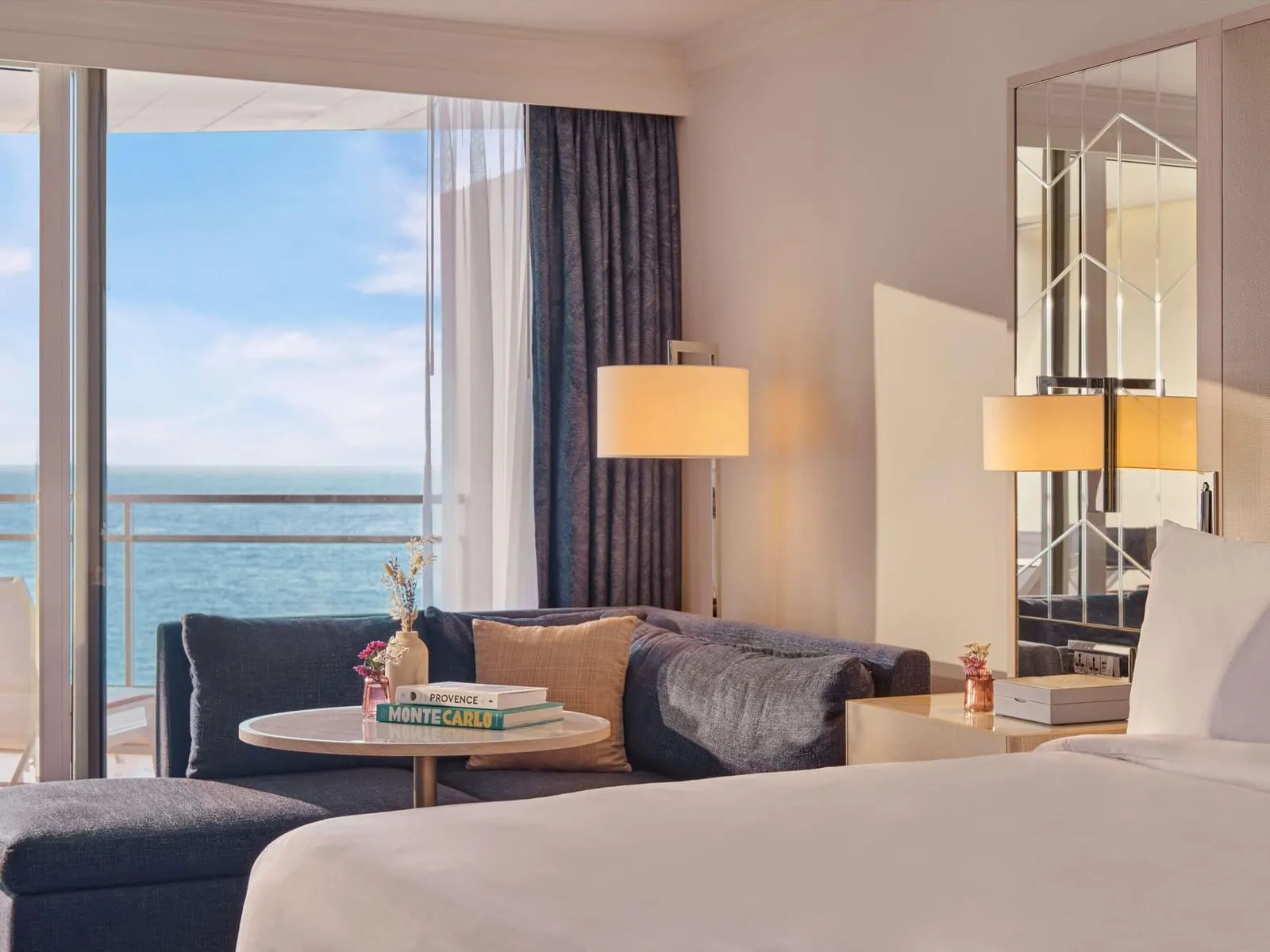 Signature Sea View room at Fairmont Monte Carlo: the sofa and a round table by the window, the sea beyond the terrace