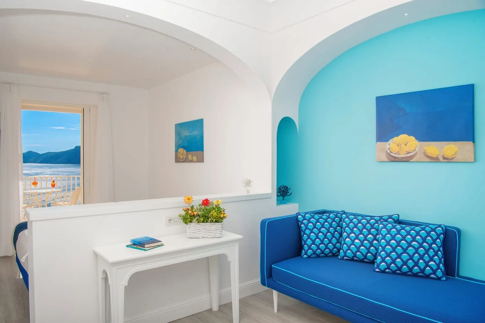 Junior Suite with terrace overlooking the sea all'Hotel Tramonto d'Oro: un divano blu in un'alcova turchese, con la zona notte dietro un muretto e porte sulla terrazza e sul mare.