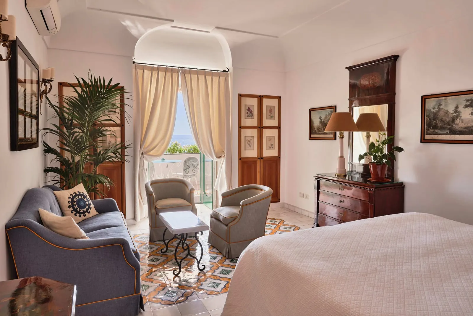 Deluxe Sea View at Le Sirenuse: a bed facing a sofa and two armchairs, with a curtained door to the balcony