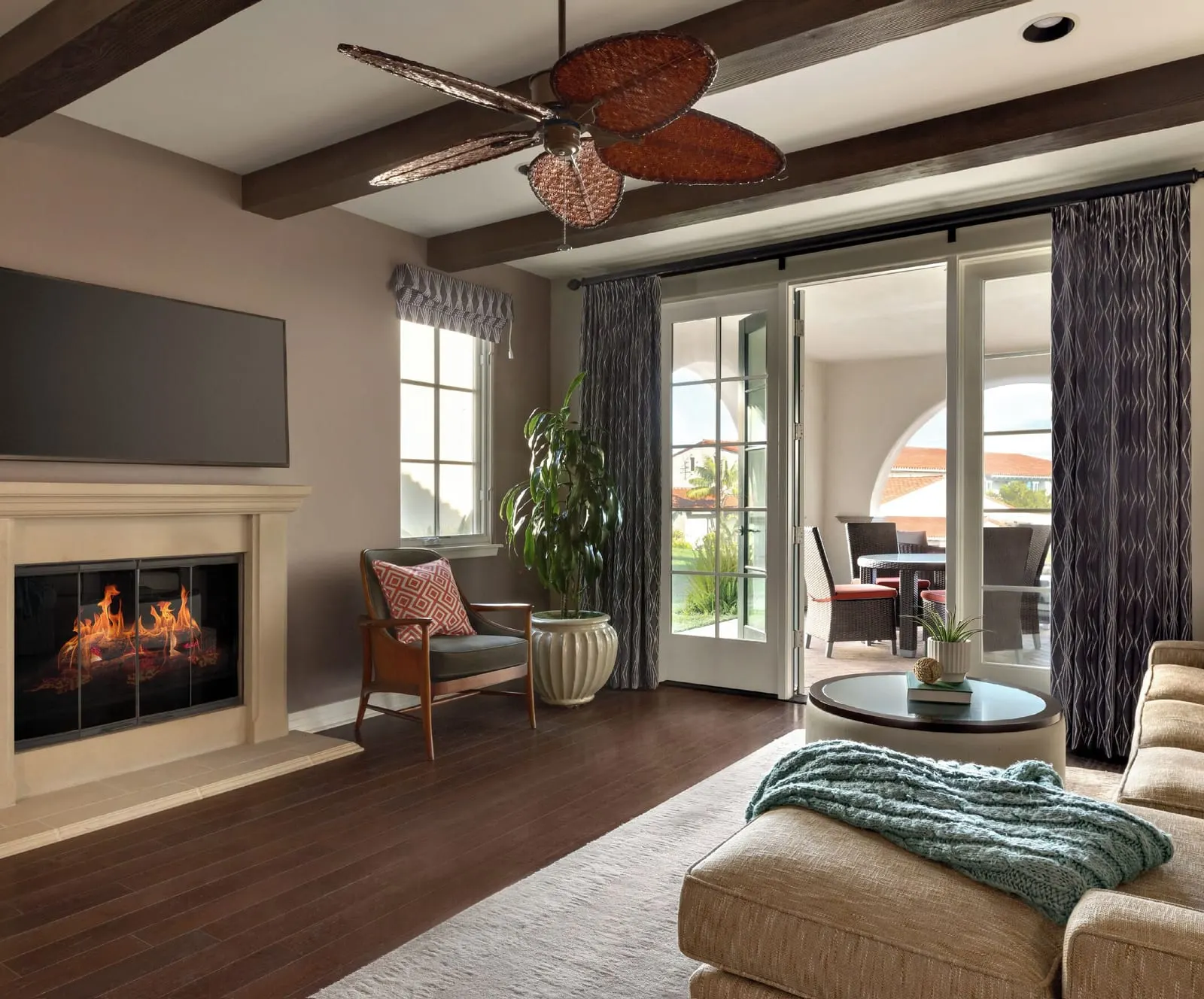 One-Bedroom Bungalow at Terranea Resort: a living room with a fireplace, a wall-mounted television, a sofa and glass doors onto a covered patio, under a beamed ceiling with a woven-blade fan
