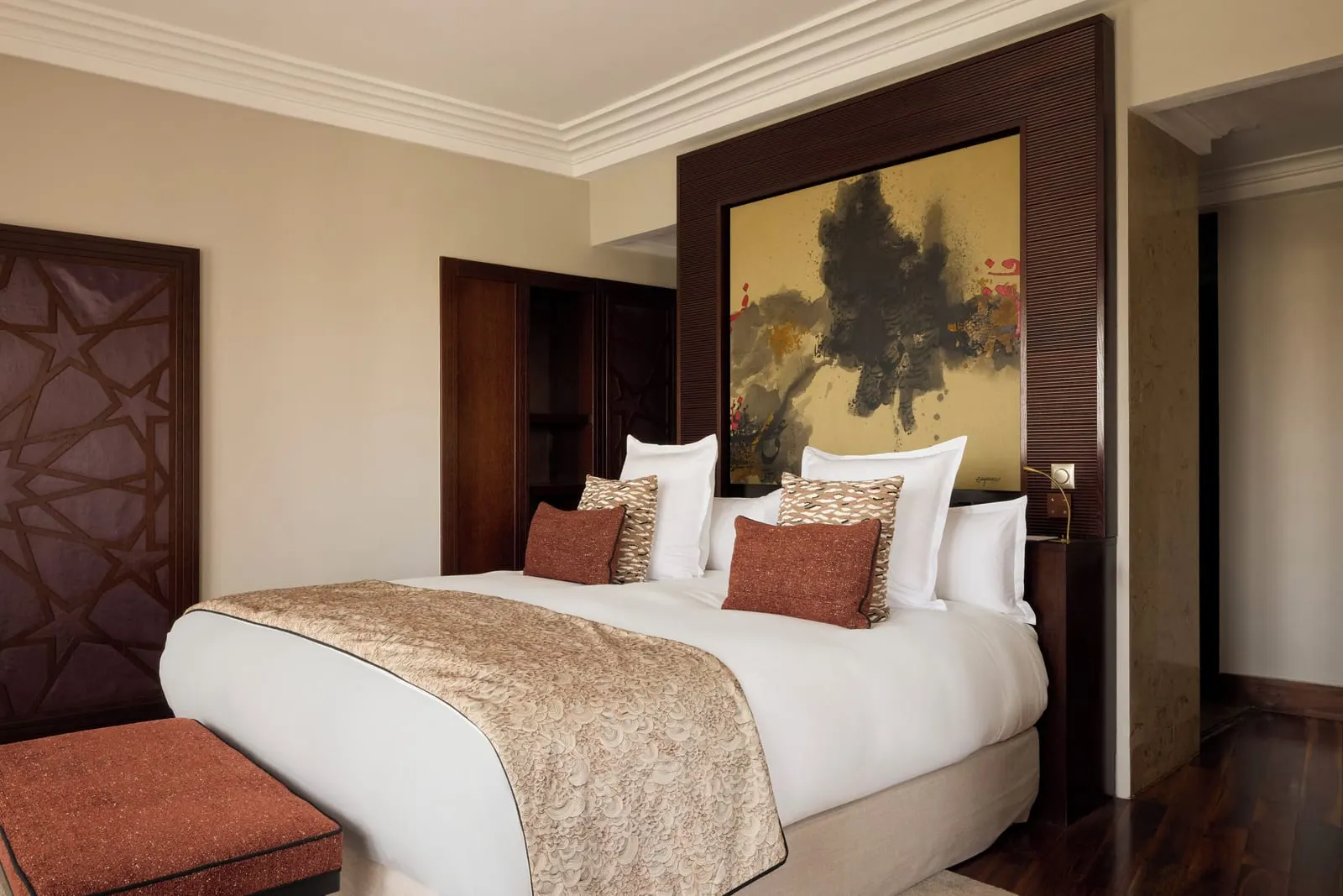 Deluxe One Bedroom Suite at Nobu Hotel Marrakech: a king bed with rust cushions before a gold and black painted headboard panel, beside a carved wooden door