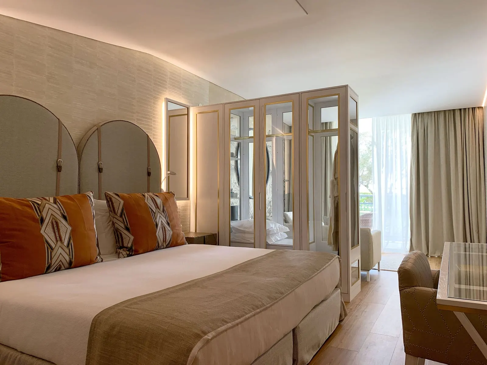 Premier Junior Suite Sea View at VidaMar Resort Hotel Madeira: a bed with arched headboards and orange cushions, a glass-fronted wardrobe and an armchair by the window