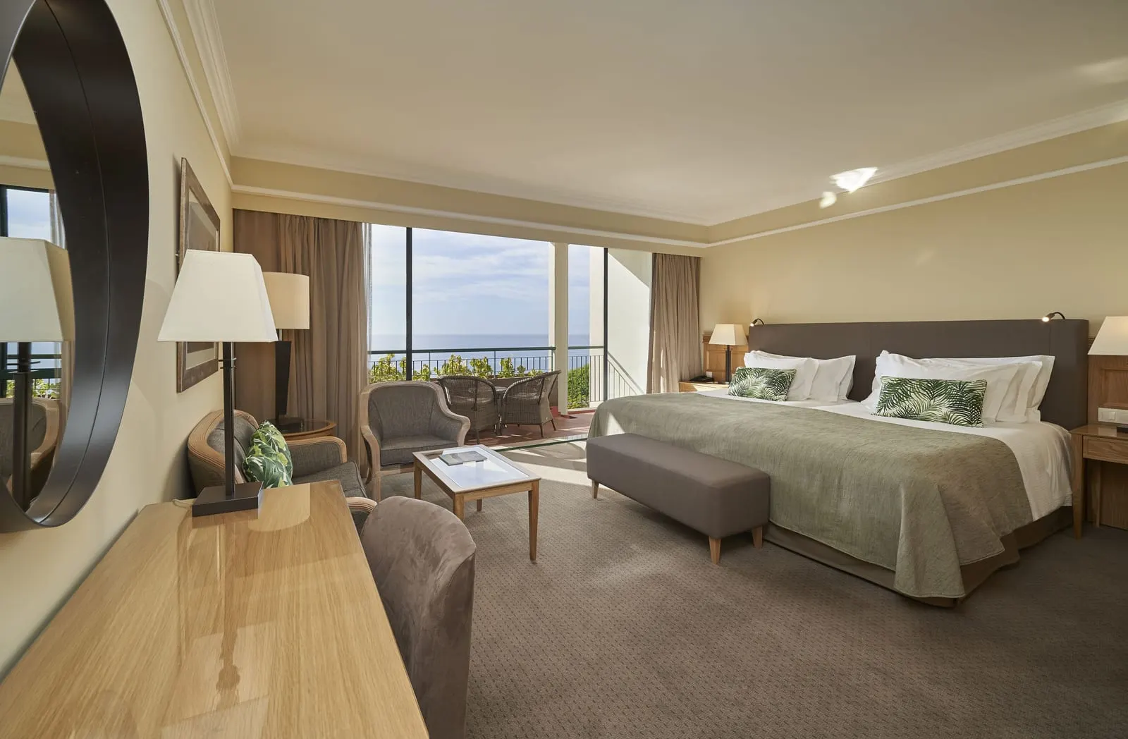 Sea View at The Cliff Bay, by PortoBay: twin beds pushed together, a sofa, armchairs and a desk with a round mirror, and a balcony with wicker chairs over the open sea