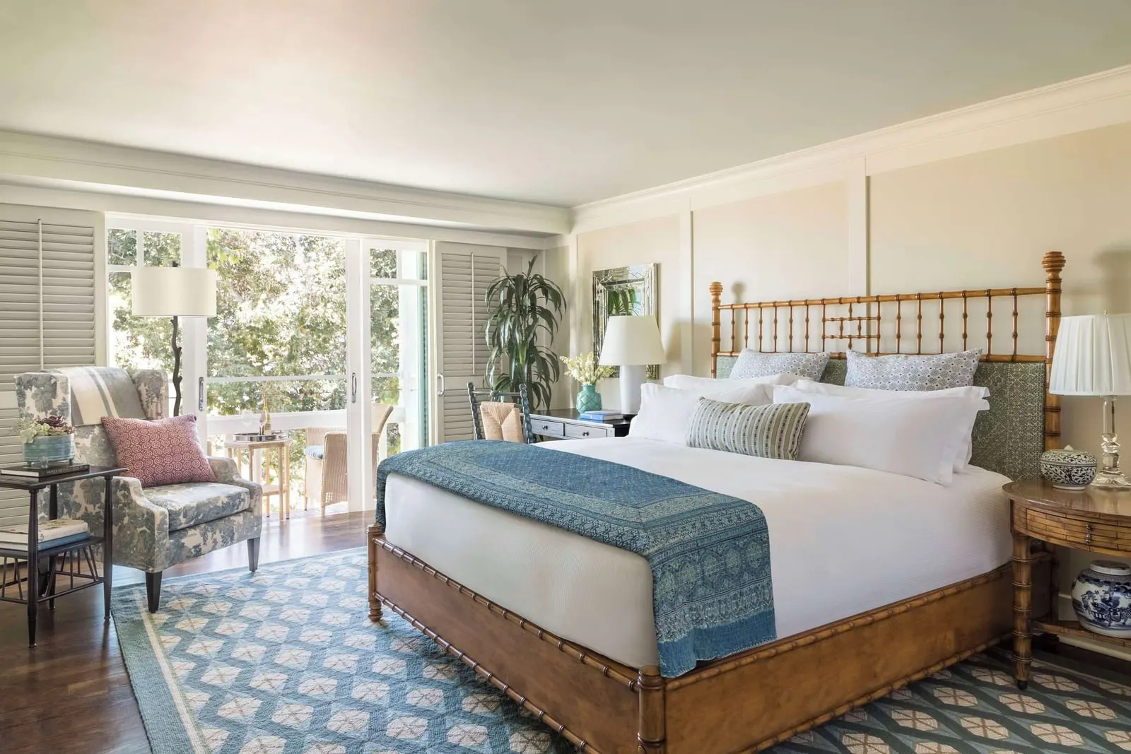 Deluxe Room im Shutters on the Beach: ein Kingsize-Bett mit einem Holzrahmen im Bambusstil und einer blau gemusterten Tagesdecke, ein Sessel mit Blumenmuster und Glastüren zu einem Balkon