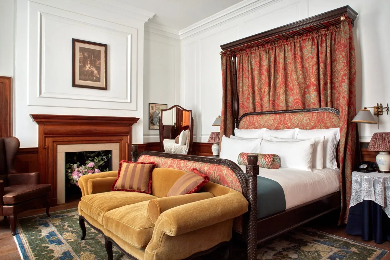 Heritage room at The Ned: a canopy bed with paisley drapes, a yellow velvet sofa and a fireplace with a wooden surround