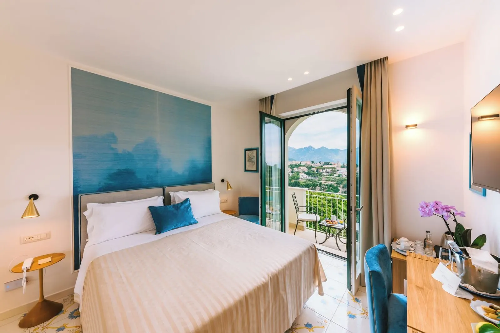 Premium Room VIOLA at Palazzo Pascal: a double bed with a blue painted headboard panel and glass doors open onto a small balcony over the hills
