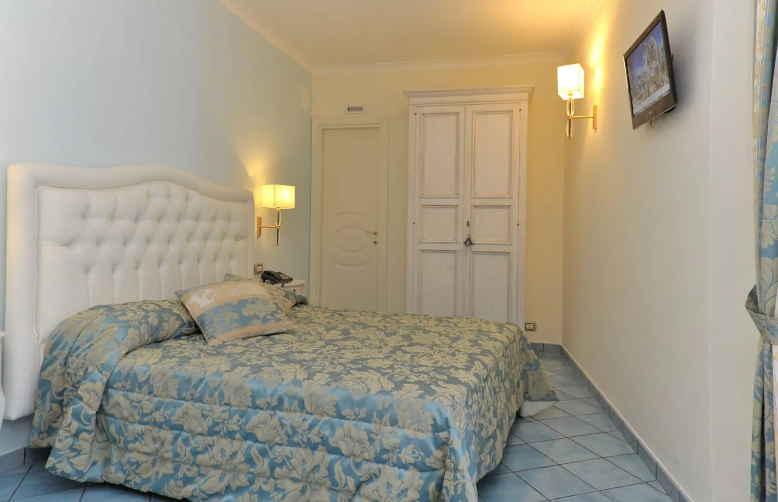 Mini Suite at Hotel Santa Lucia: a double bed with a buttoned white headboard and a blue floral cover, with a white wardrobe beyond