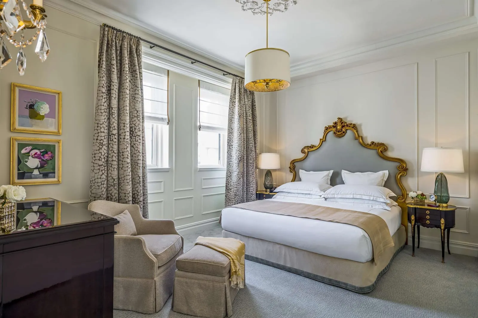 Penthouse One Bedroom Suite King at The Plaza: a king bed with a gilded grey headboard, a tub chair with a footstool, two framed floral paintings and a dark wood dresser