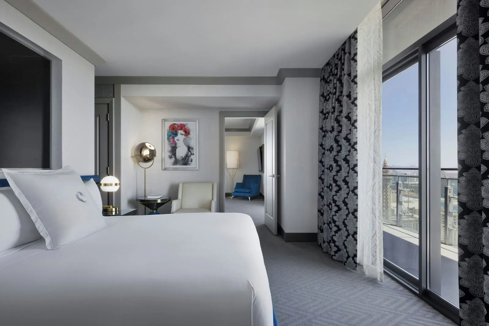 Wraparound Terrace Suite at The Cosmopolitan of Las Vegas: the bedroom, with a king bed, a cream armchair and full-height glass doors hung with black and white patterned curtains