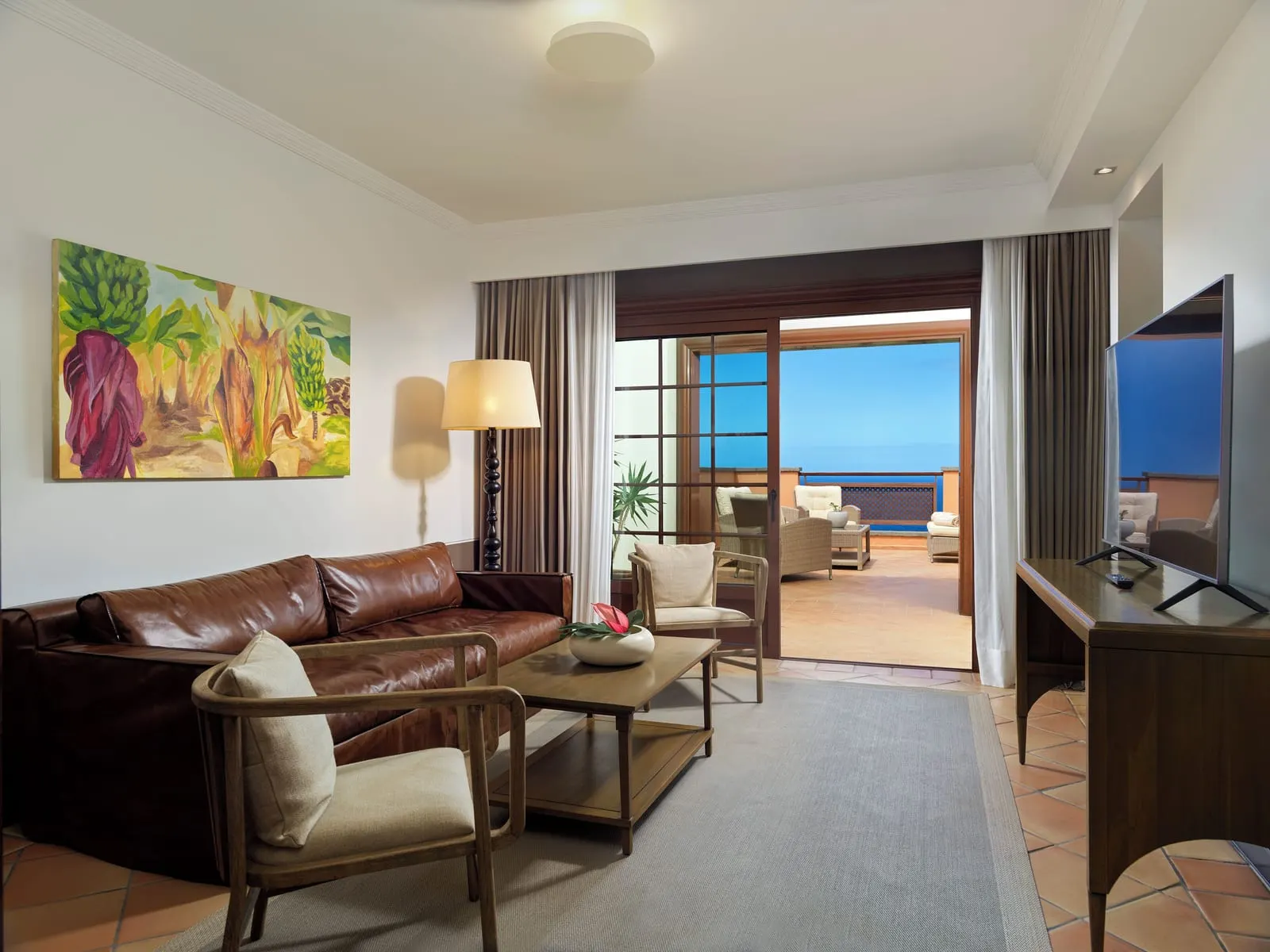 Suite Sea View at Hacienda del Conde: the living room, a leather sofa and doors open to the terrace and the sea