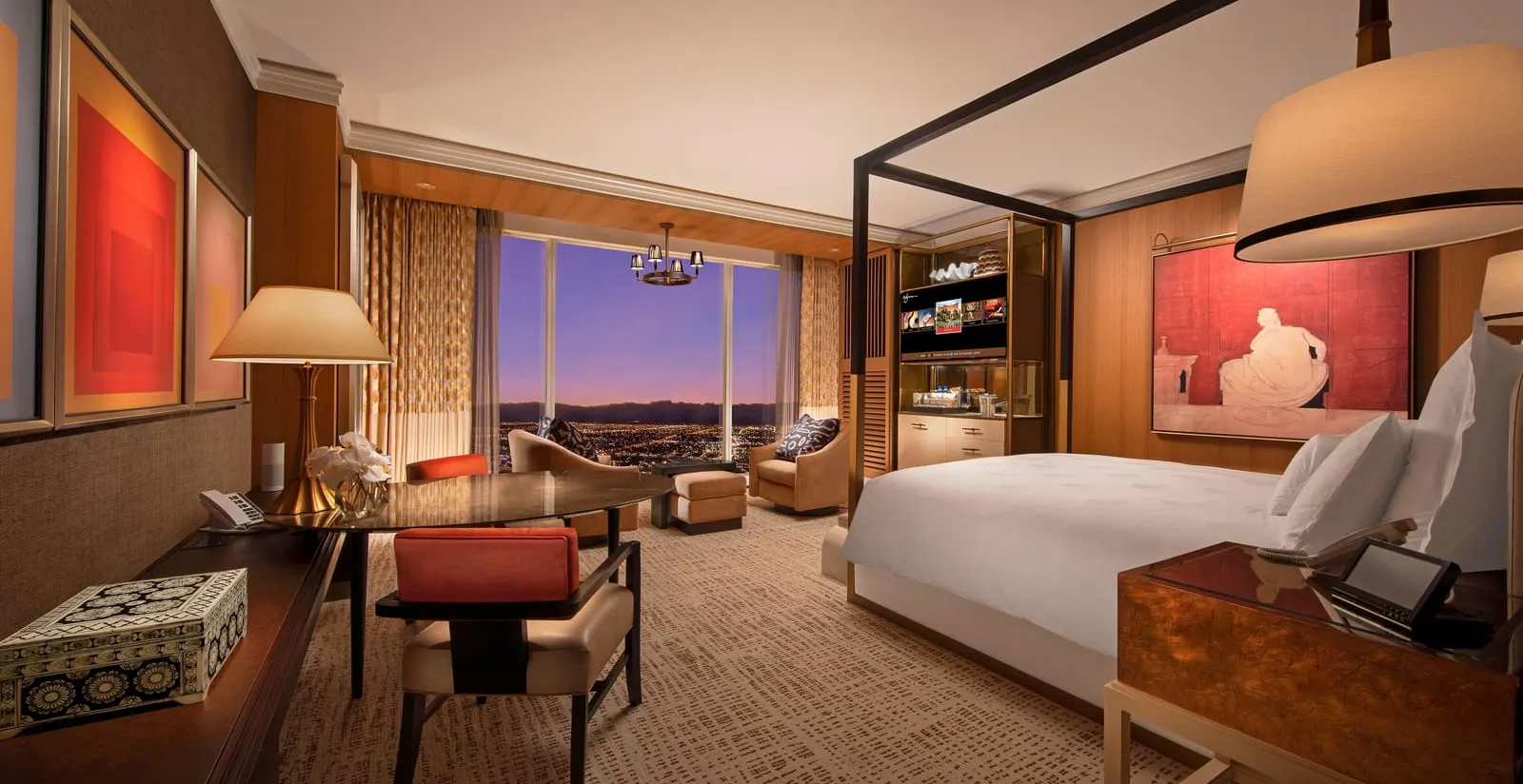 Wynn Tower Suite King at Wynn Las Vegas: a king bed under a canopy frame, an oval table with two orange-backed chairs, and two armchairs and a footstool by a floor-to-ceiling window