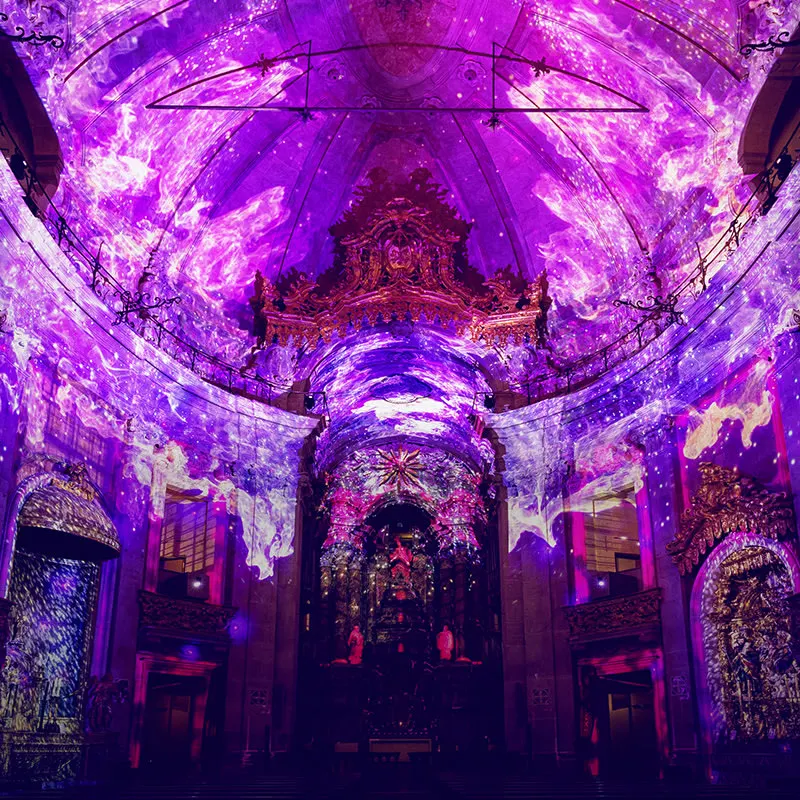 The nave and dome of the Clérigos Church in Porto washed in purple and pink projections during Spiritus, with the gilded altar lit below