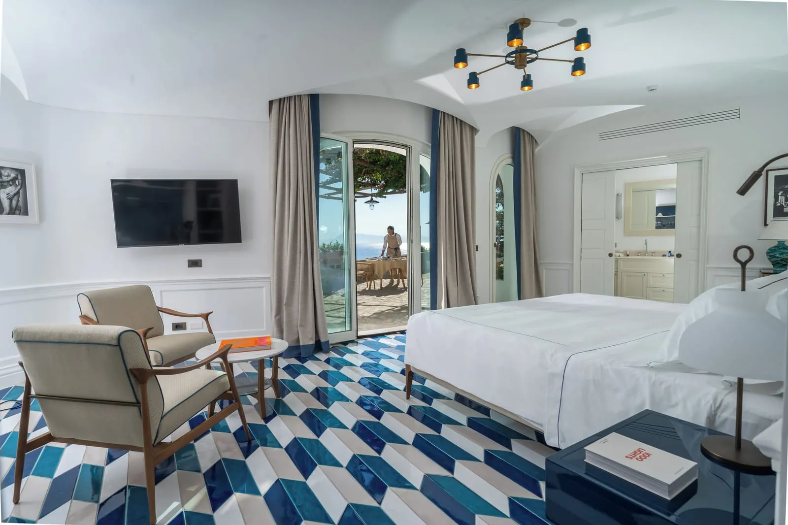 Junior Suite Sea View & Pool at Borgo Santandrea: a king bed and two armchairs, with glass doors open to a sunny terrace.