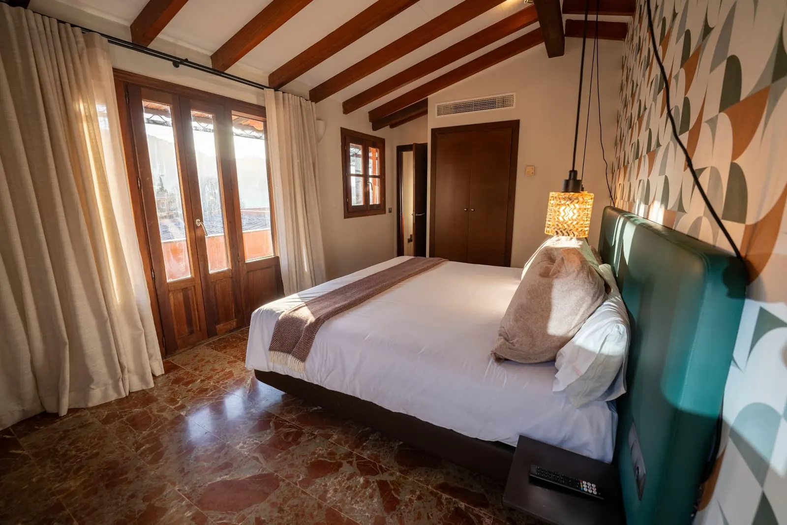 Suite Penthouse at Maristel Hotel & Spa: a bed with a green headboard under a beamed ceiling, with a red marble floor and tall glazed doors
