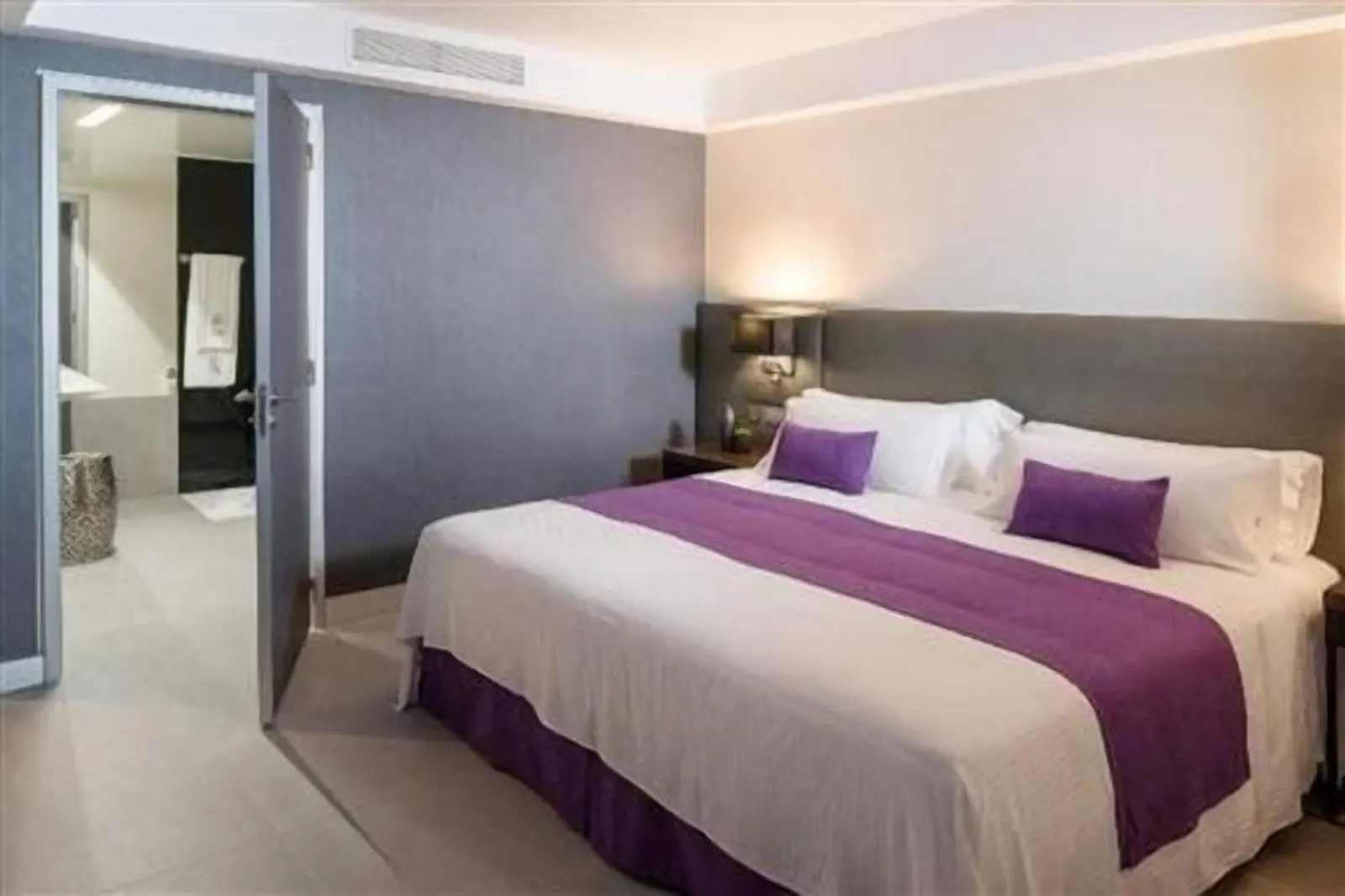 Classic Suite Superior at La Isla y el Mar Hotel Boutique: a king bed with a purple runner and an open bathroom door beside it