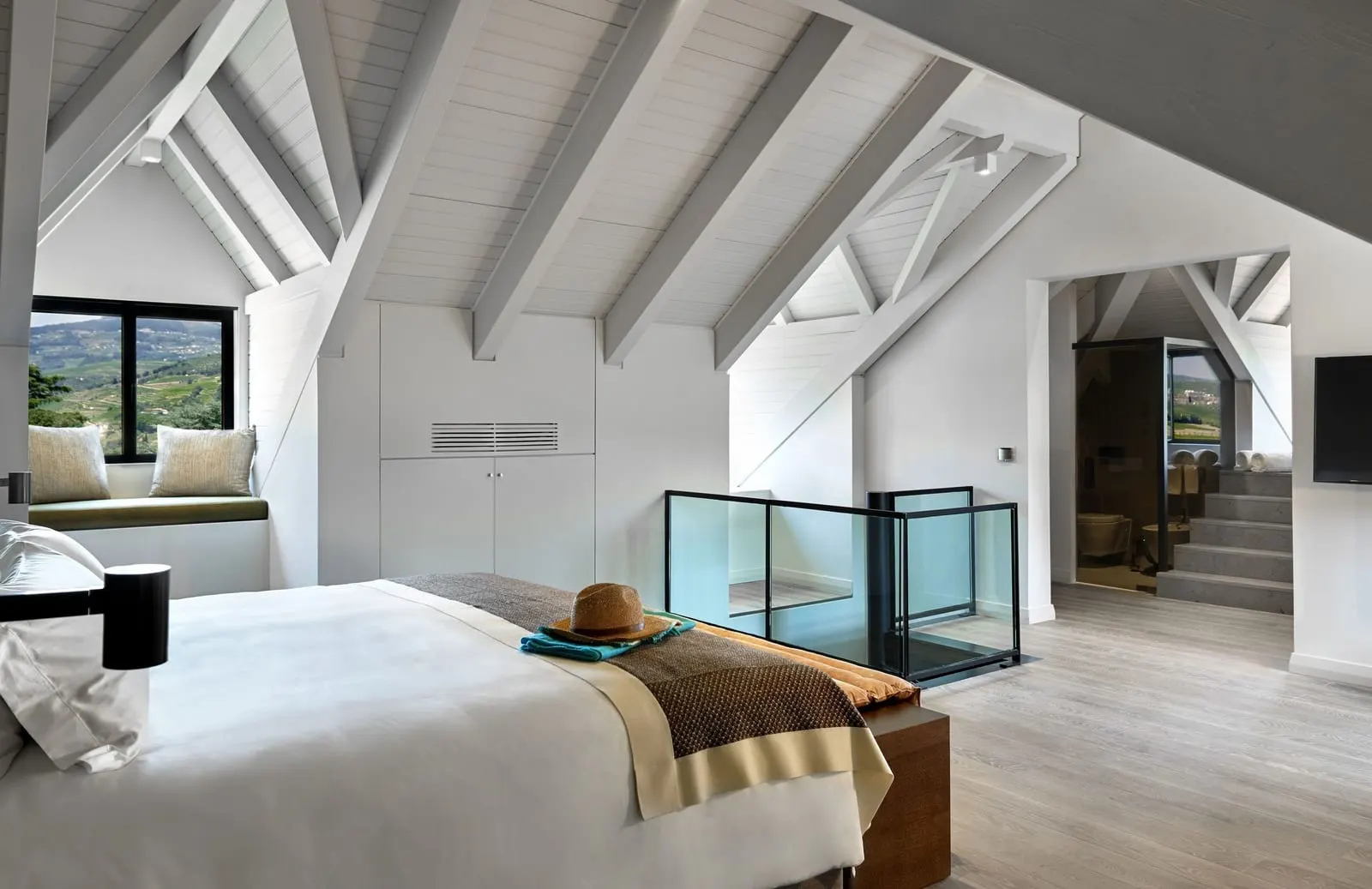 Quinta Duplex Suite at Six Senses Douro Valley: the upstairs bedroom under white roof beams, beside a glass-sided stairwell