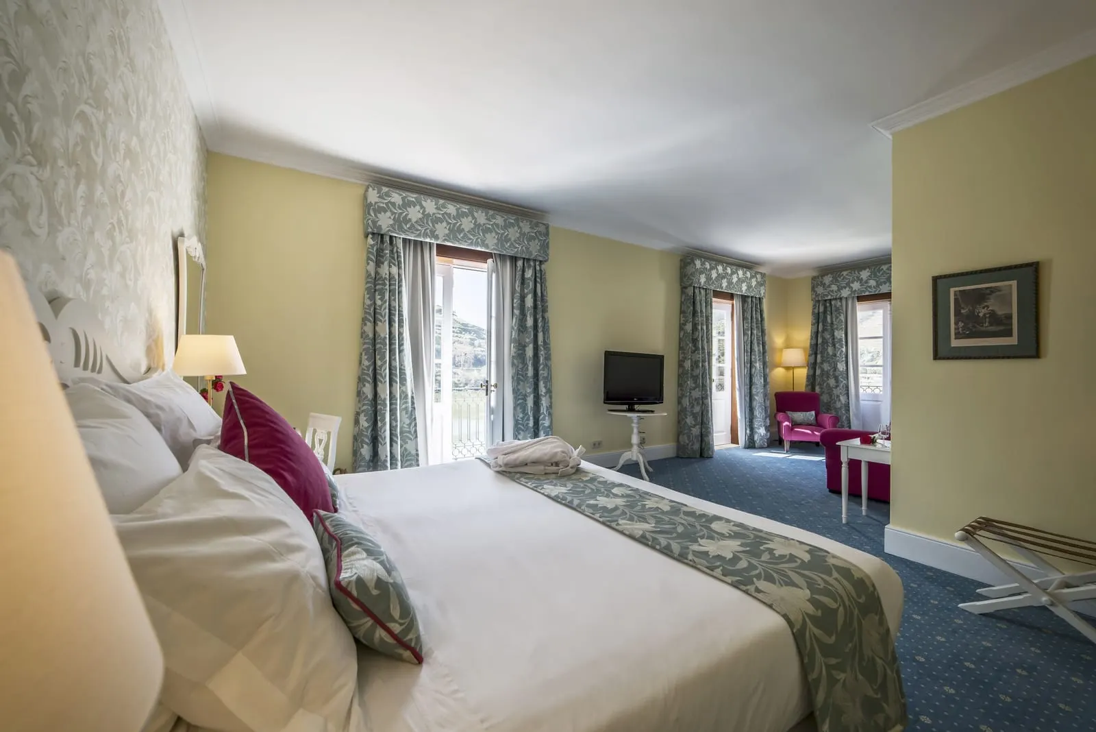 Junior Suite Douro River View at The Vintage House: the bed, three tall curtained windows and a pink armchair at the far end