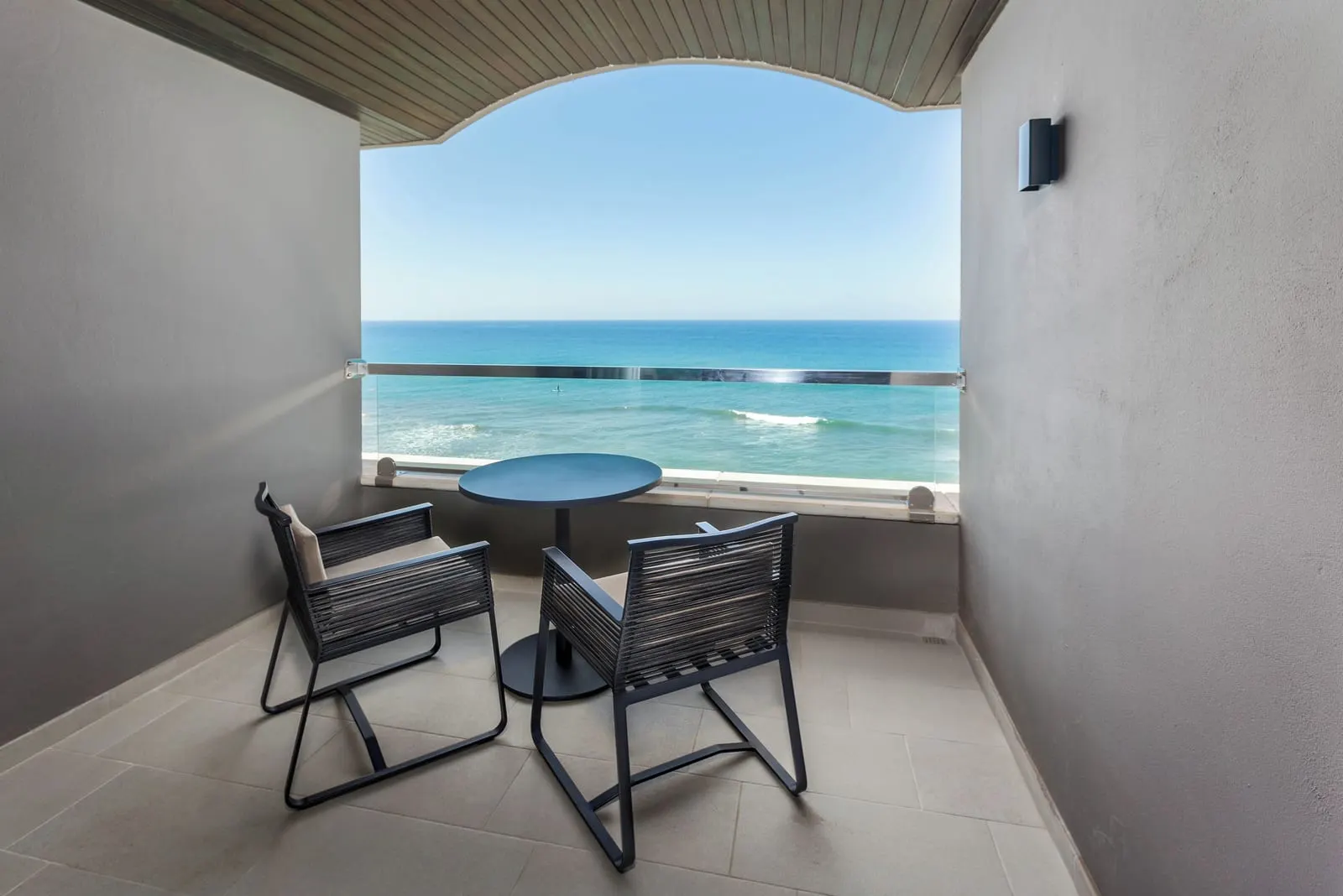 Double Superior View at Hotel Faro, a Lopesan Collection Hotel: a covered balcony with a round table and two chairs behind a glass balustrade, facing straight out to sea