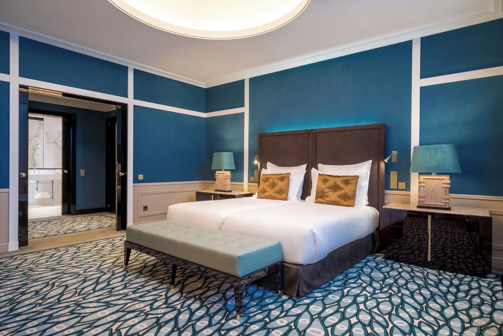 Porto Suite bedroom at The One Monumental Palace: the bed with a bench, blue walls and an open door to the marble bathroom
