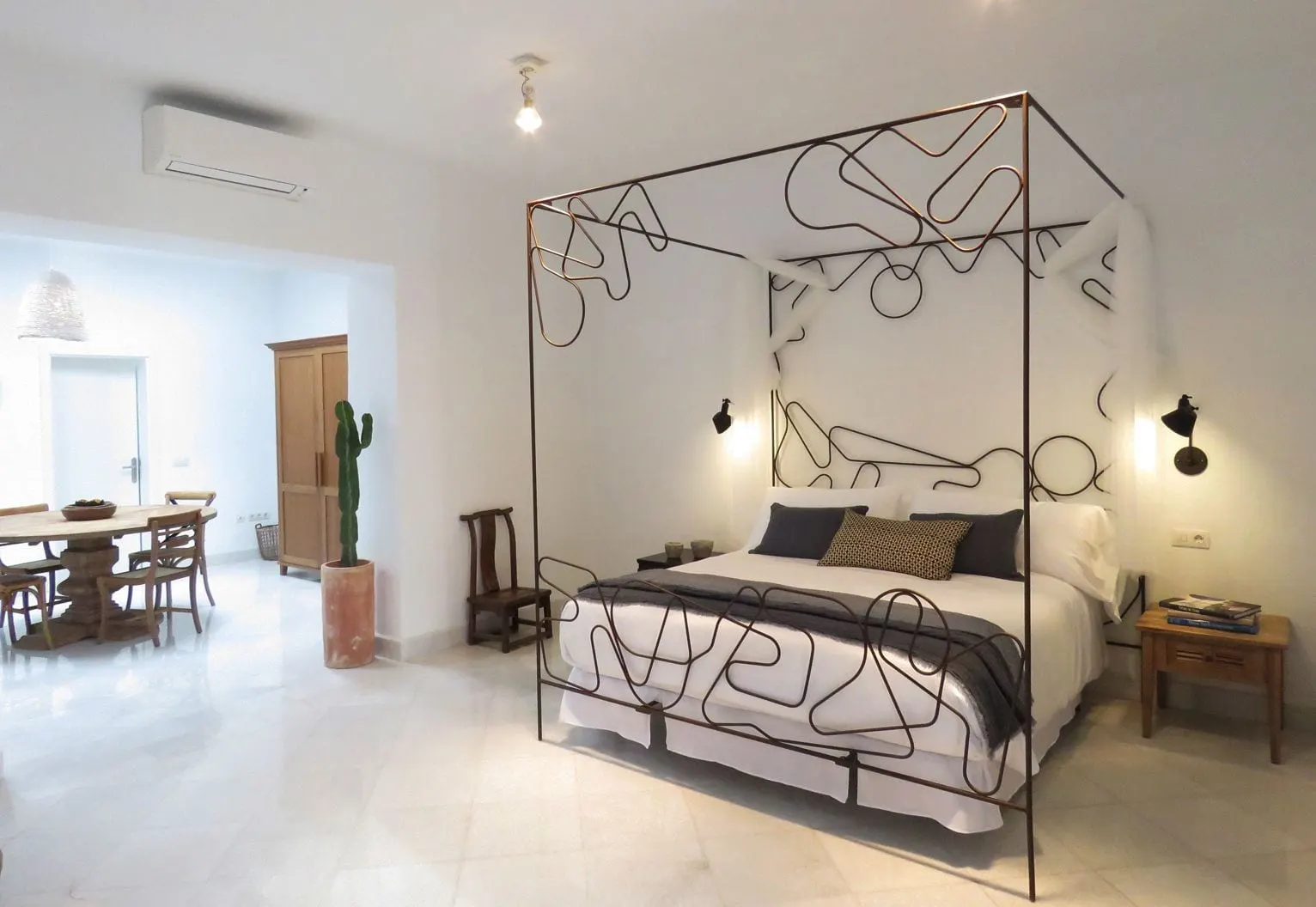 Suite 05 at Hotel Boutique Palacio Ico: a bed with a wrought metal canopy and a dining table in the room beyond, on white marble floors