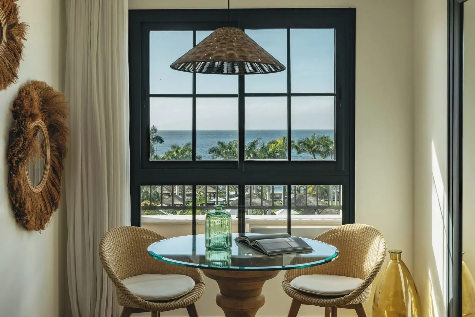 Deluxe Ocean Front View at Gran Meliá Palacio de Isora: a glass table and wicker chairs at a window onto palms and the sea