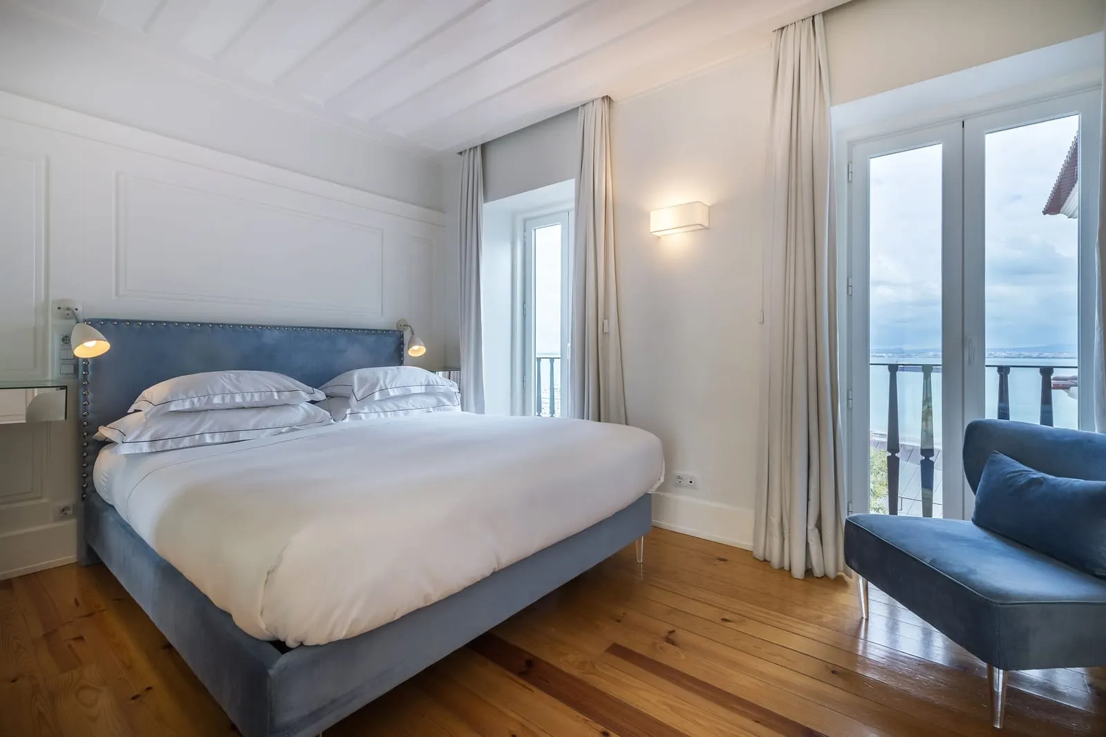 Classic River Bedroom at Santiago de Alfama: the double bed, a blue armchair and French windows with a railing over the river