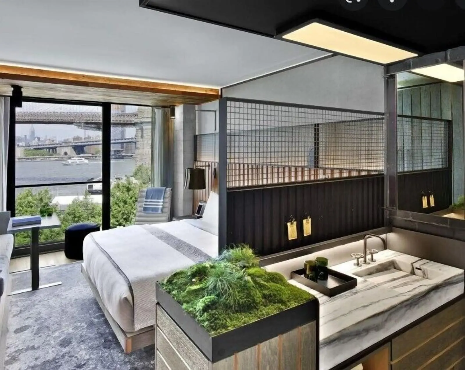 Bridge King at 1 Hotel Brooklyn Bridge: a king bed beside an open marble washbasin with a moss planter, and a sliding window onto the Brooklyn Bridge and the East River