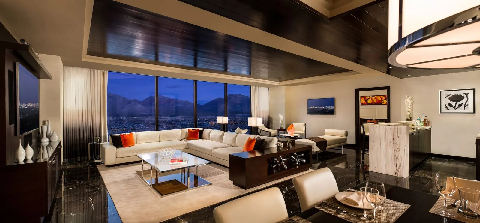 One Bedroom Luxury Suite at Red Rock Casino Resort & Spa: the parlour, with an L-shaped cream sofa, a glass coffee table, a bar counter with a pale stone front, a dining table in the foreground and a wall of windows