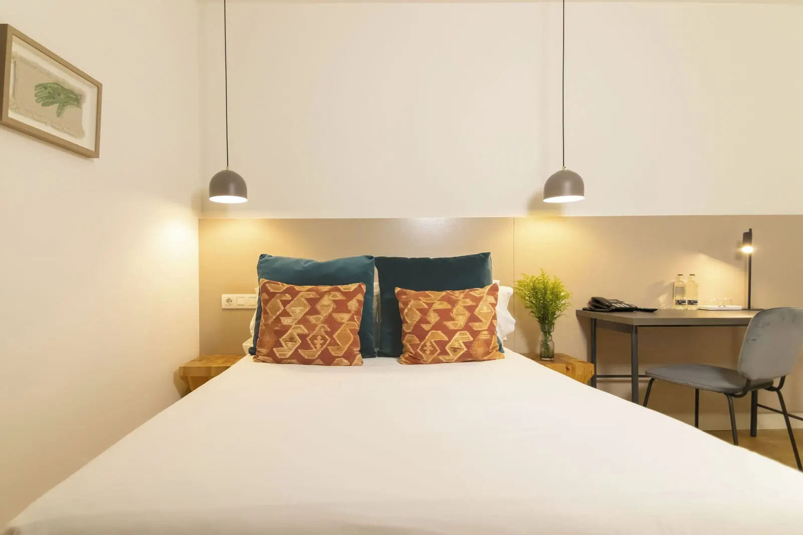 Single Classic at Hotel Veintiuno: a bed with teal and orange patterned cushions under two grey pendant lamps, beside a small desk with a telephone and a grey chair