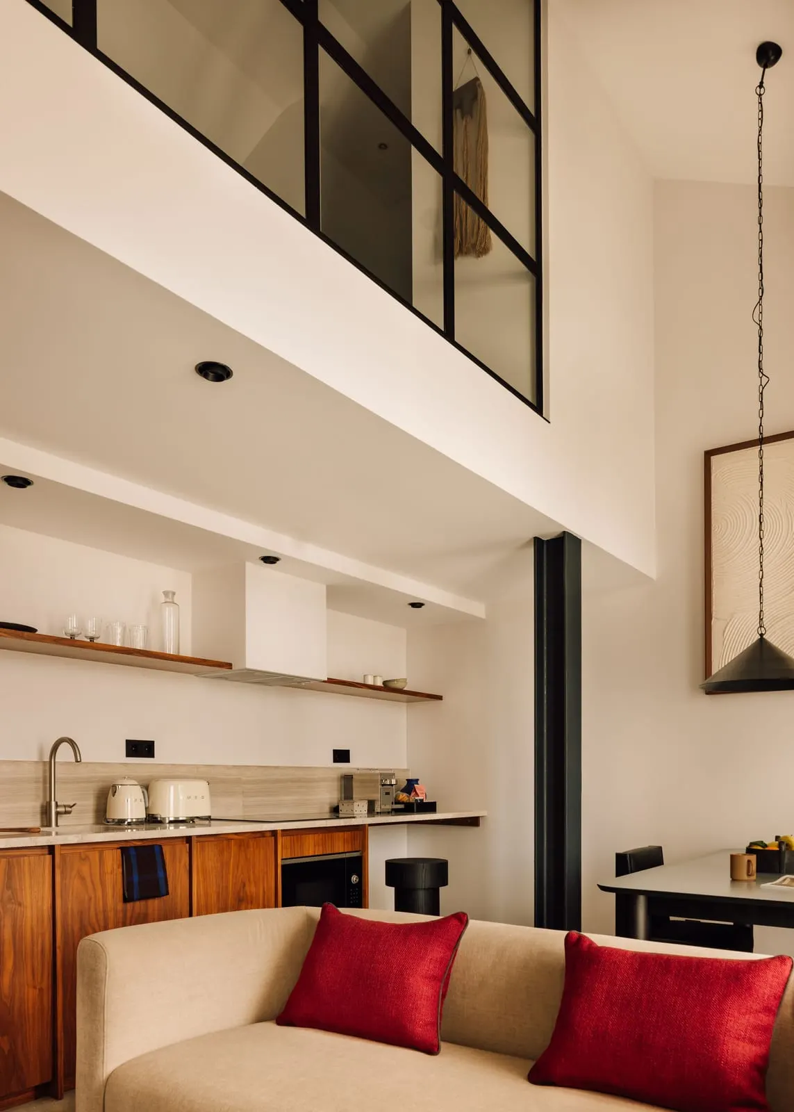 One Bedroom Duplex River Suite at The Rebello: the living room with a sofa and the kitchen, below the glazed upper floor
