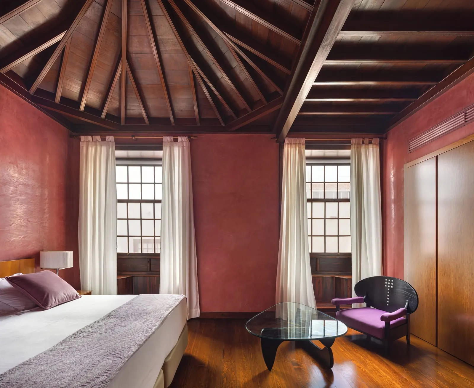Double Collection room at Hotel San Roque: red walls, two tall windows, a glass table and a purple armchair