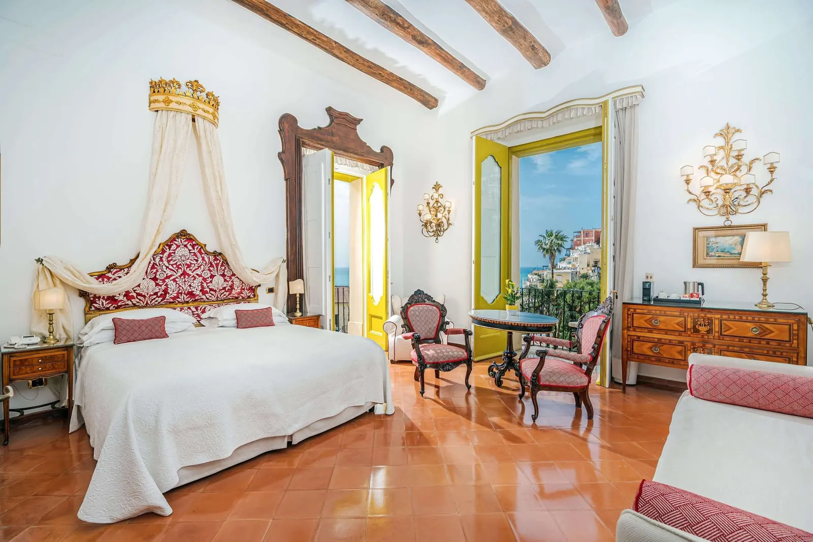 Special Deluxe Sea View im Palazzo Murat: ein Bett mit Krone und rotem Damastkopfteil, antike Stühle, ein runder Tisch und zwei hohe Fenster