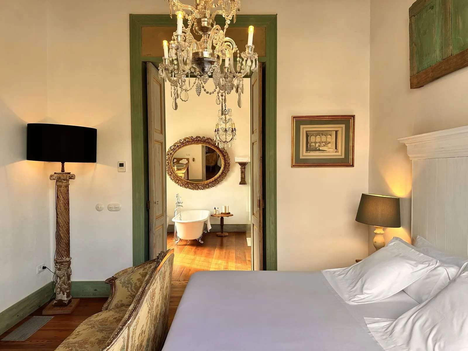 Room Nº1. Sup.Double at La Casa de los Naranjos: a bed under a chandelier, with a green-framed doorway opening to a second room with a freestanding bath