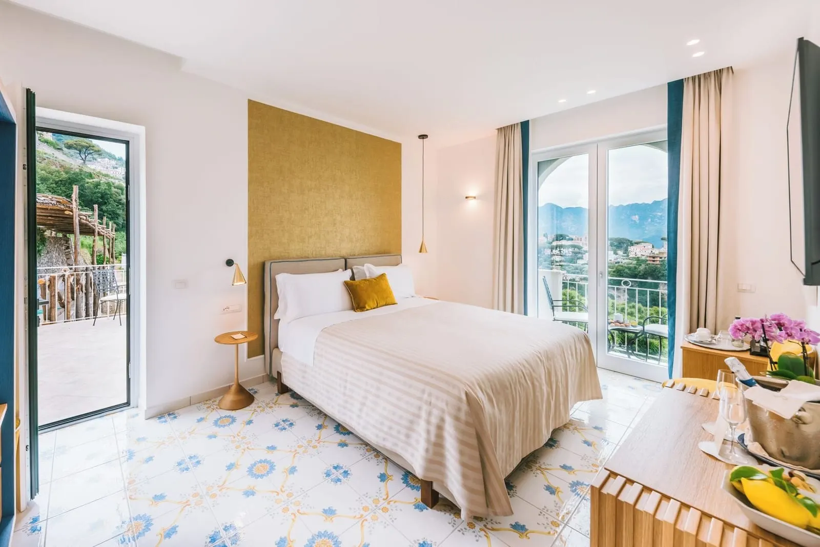 Deluxe Room TIGLIO at Palazzo Pascal: a double bed with a gold headboard wall and glass doors open onto the outdoor space