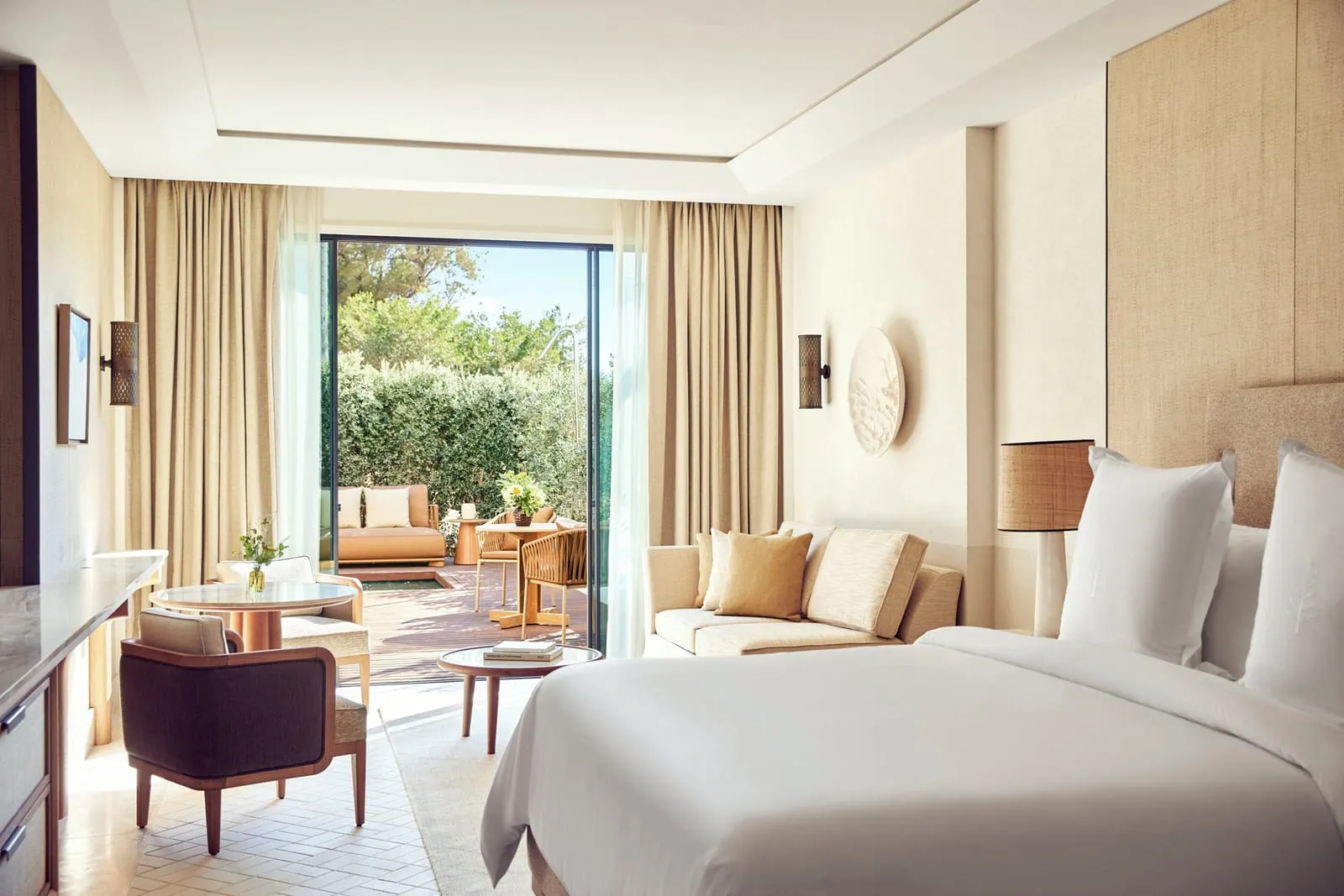 Garden-View Room with Plunge Pool at Four Seasons Resort Mallorca at Formentor: a bed with white linen, a sofa and an armchair, facing open glass doors onto a terrace with a daybed and clipped hedges