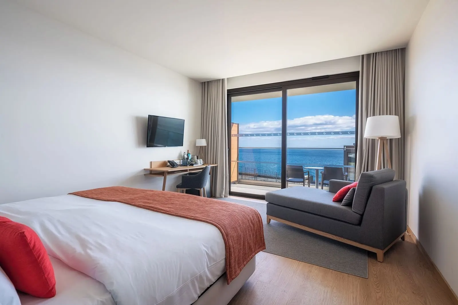Double Room Cliff Balcony at Sentido Galomar: a double bed with a rust throw, a grey chaise longue and a glass door to a balcony with chairs above the sea